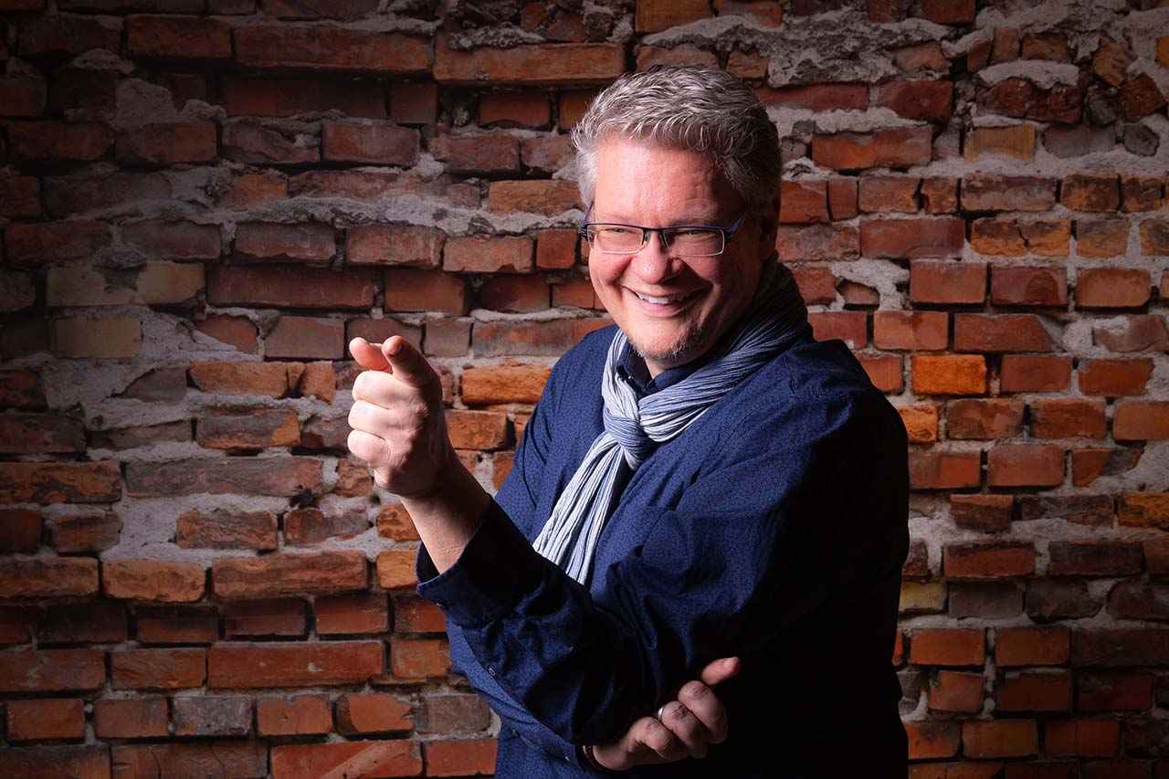 Lutz vor einer Steinwand zeigt auf dich